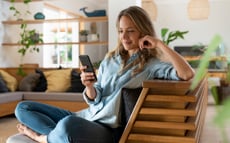 Eine Dame sitzt lächelnd auf der Couch und schaut auf ihr Telefon